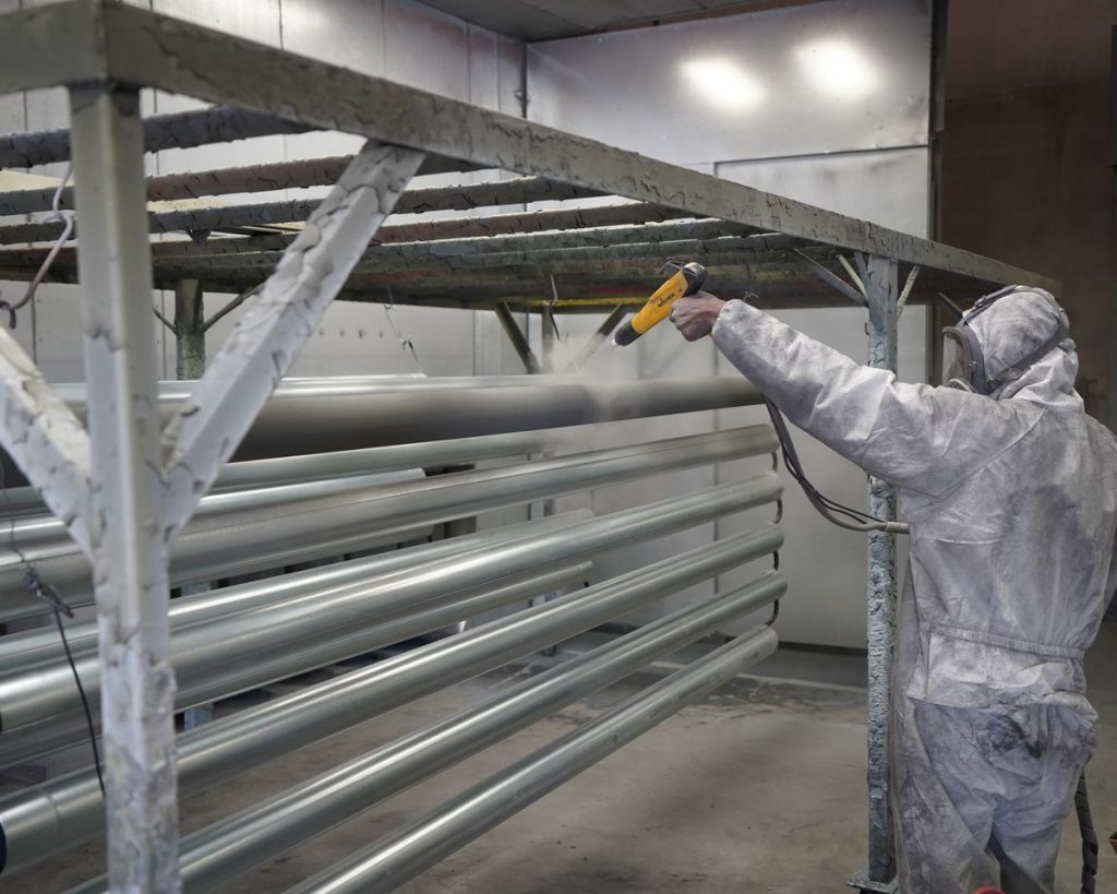 Worker powder coating metal tubes in a spray workshop
