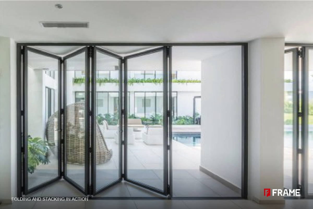 Aluminum folding door leaves stacking in a Z-fold against the frame of a poolside opening